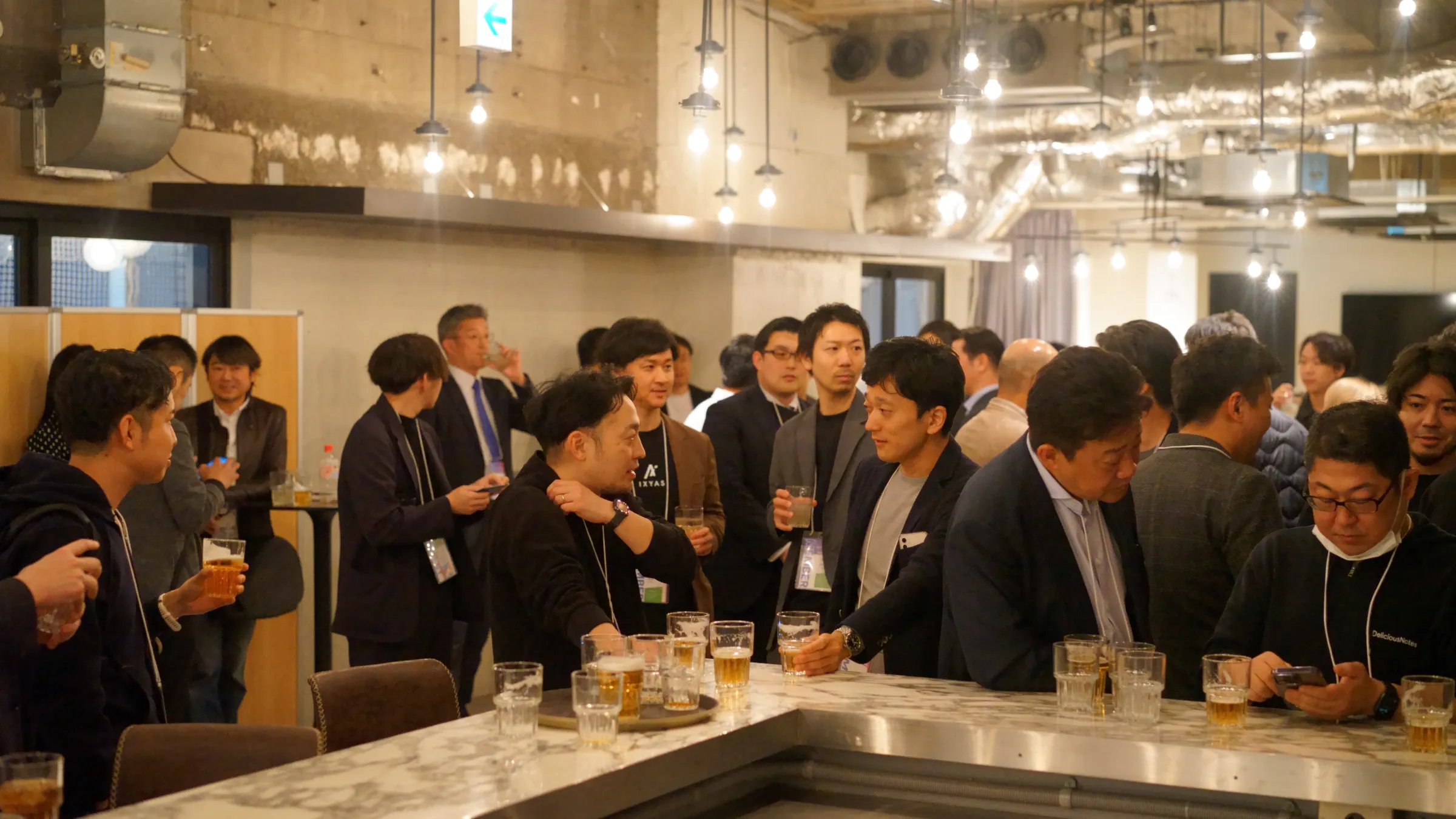 2025年3月の総会・懇親会で、懇親会で、カウンターの前で話す参加者